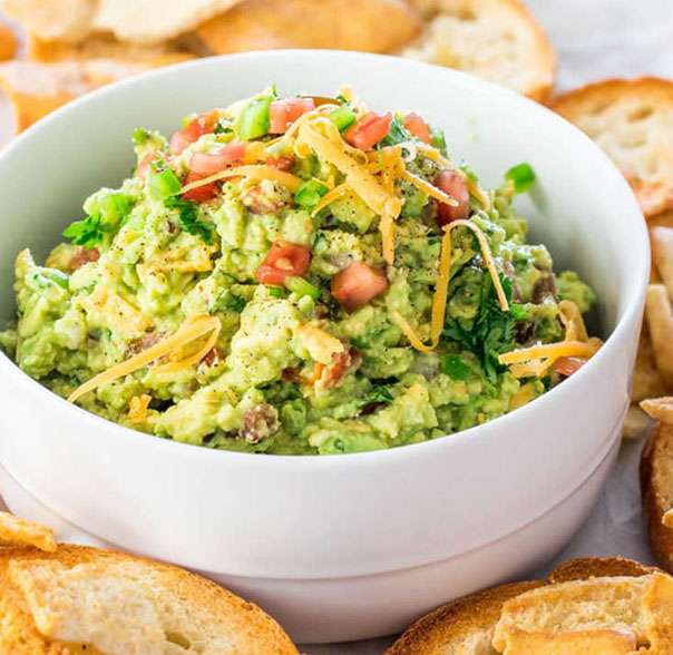 A bowl of guacamole with chips and crackers.