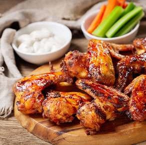 Bbq chicken wings on a wooden cutting board with carrots and celery.
