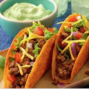 Three tacos on a plate with limes and salsa.