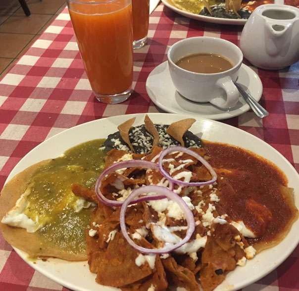 A plate of mexican food on a table with orange juice.
