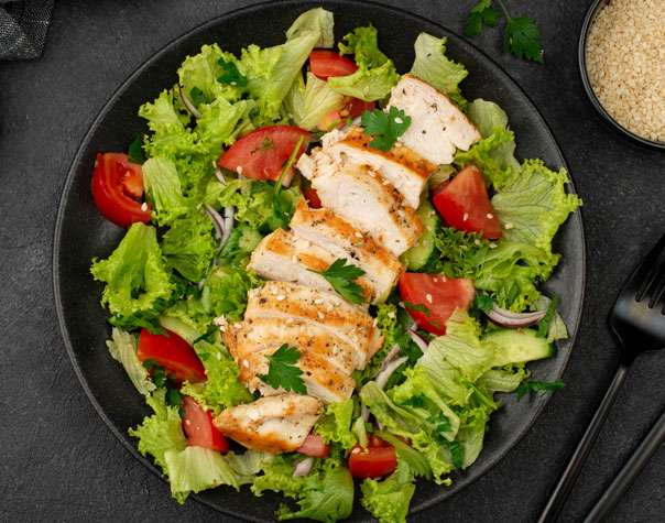 A salad with chicken and vegetables on a black plate.