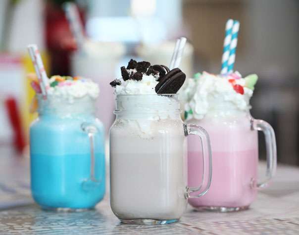 Three milkshakes in mason jars are lined up on a table.