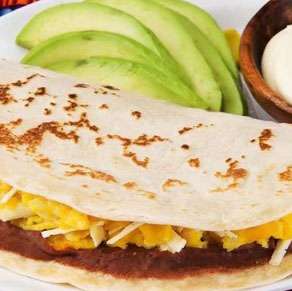 A mexican breakfast burrito on a plate with guacamole and avocado.
