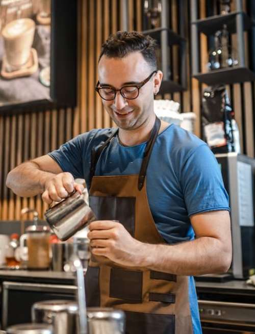 A young man pouring coffee in a coffee shop.