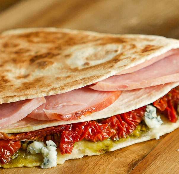 A ham and blue cheese quesadilla on a wooden cutting board.