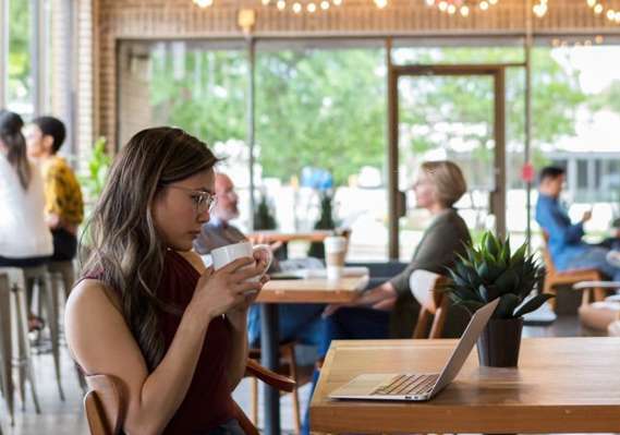 A woman sitting at a table in a coffee shop with a laptop.